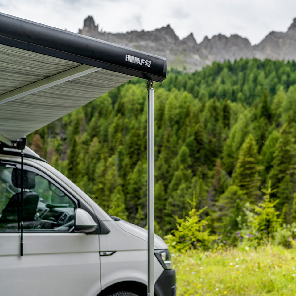 White camper van with an extended Fiamma F43 awning in a mountainous forest setting