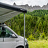 White camper van with an extended Fiamma F43 awning in a mountainous forest setting