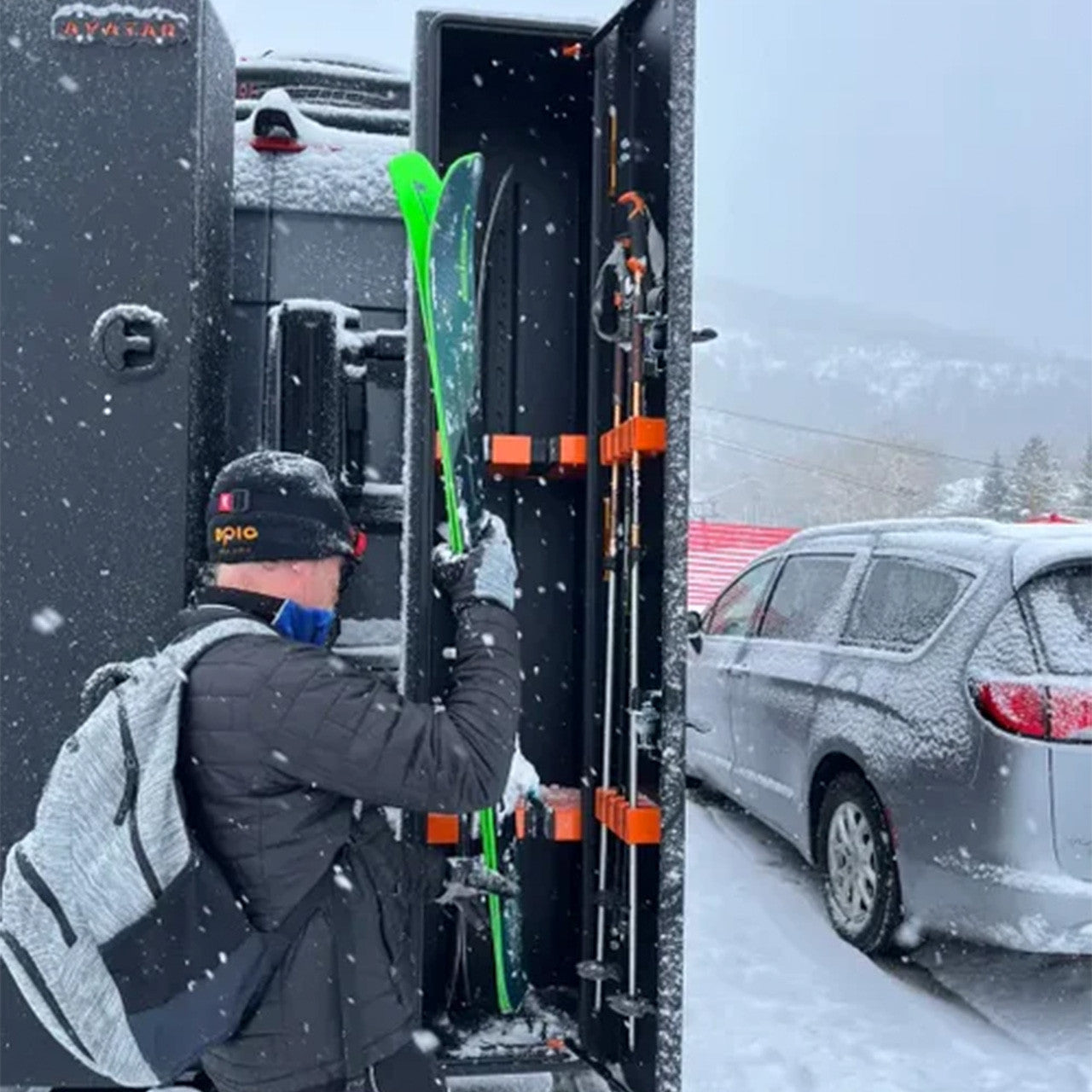 Person loading skis into a vehicle with a snowy background