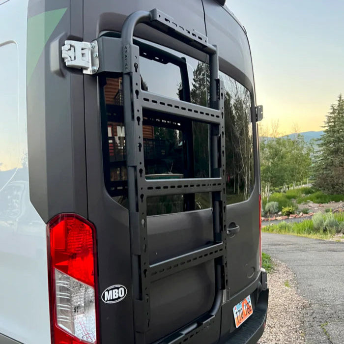 Back of a van with a ladder rack on a road with trees and sky in the background