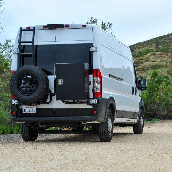 Ram ProMaster van traveling through a natural landscape during an overland trip with its rear bumper rack holding a storage box and spare tire